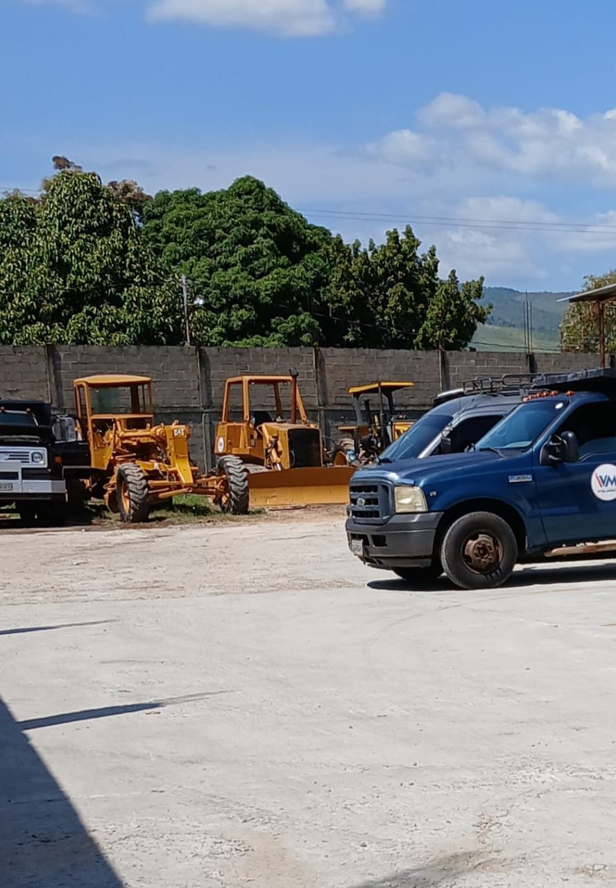 Tractores amarillos y camioneta azul con logo de la empresa frente a un muro