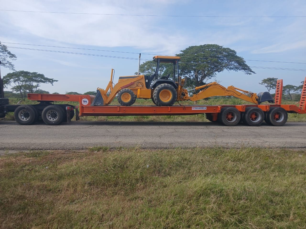 Retroexcavadora amarilla sobre plataforma low boy en carretera